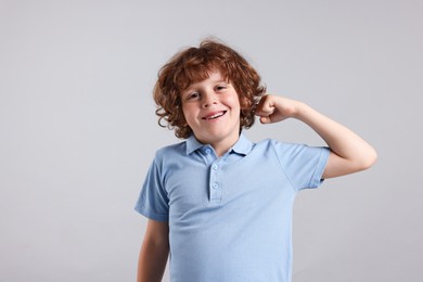 Photo of Strength. Happy little boy showing his biceps on light grey background