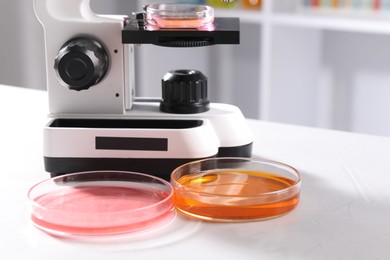 Photo of Petri dishes with different samples and microscope on white table in laboratory, closeup. Solution chemistry
