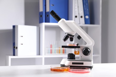Photo of Petri dishes with different samples and microscope on white table in laboratory, space for text. Solution chemistry