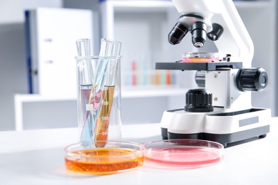 Photo of Petri dishes with different samples, test tubes and microscope on white table in laboratory, closeup. Solution chemistry