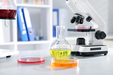 Photo of Petri dishes with different samples, flask and microscope on white table in laboratory. Solution chemistry
