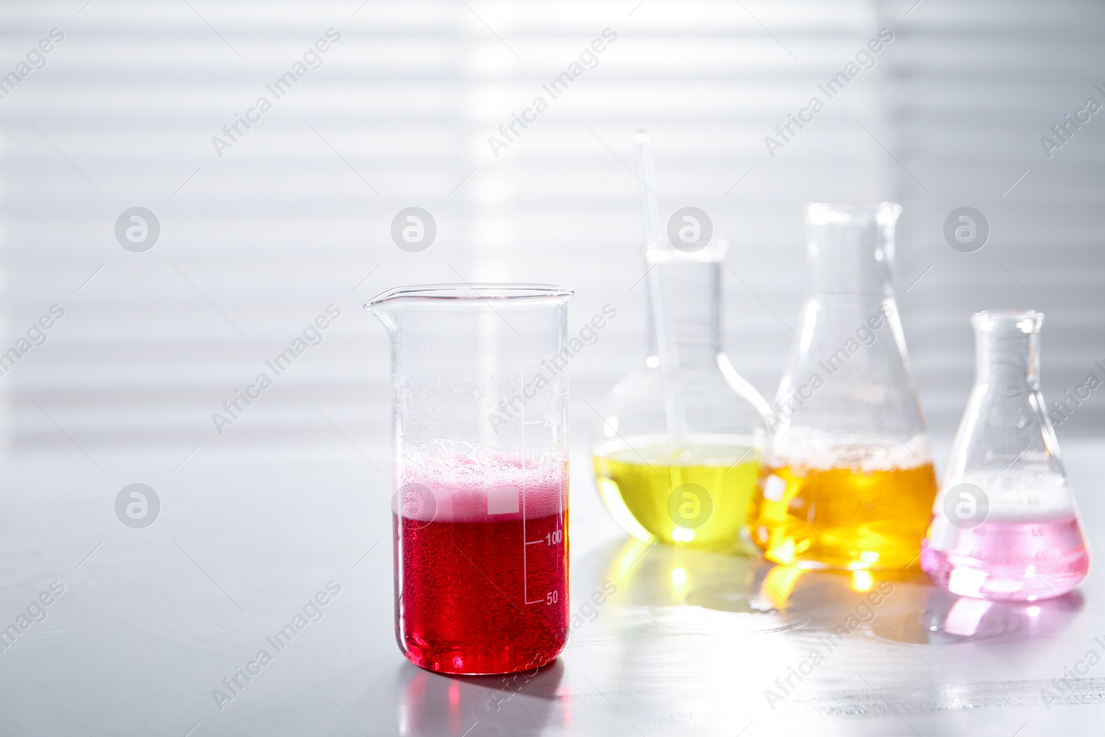 Photo of Laboratory glassware with different samples on light table indoors. Solution chemistry