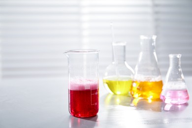 Photo of Laboratory glassware with different samples on light table indoors. Solution chemistry