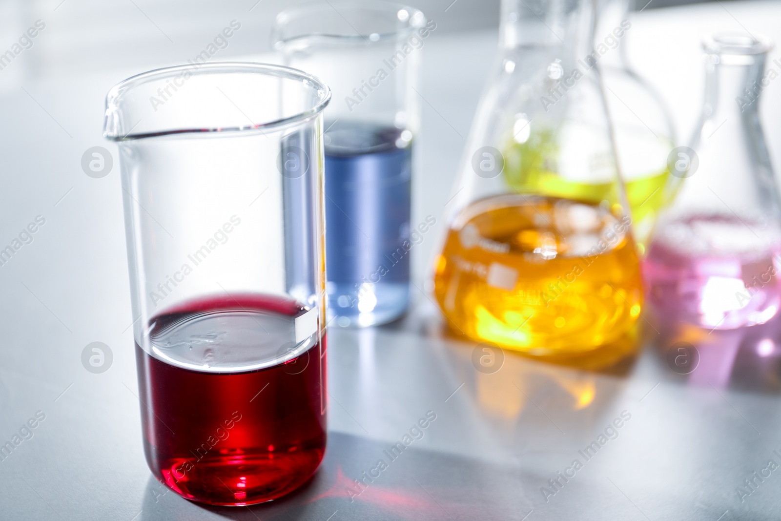 Photo of Laboratory glassware with different samples on light table indoors, closeup. Solution chemistry