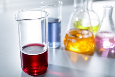 Photo of Laboratory glassware with different samples on light table indoors, closeup. Solution chemistry