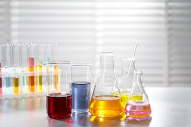Photo of Laboratory glassware with different samples and test tubes on light table indoors. Solution chemistry