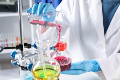 Photo of Scientist pouring sample in glass flask indoors, closeup. Solution chemistry