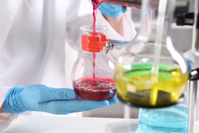 Photo of Scientist pouring sample in glass flask indoors, closeup. Solution chemistry