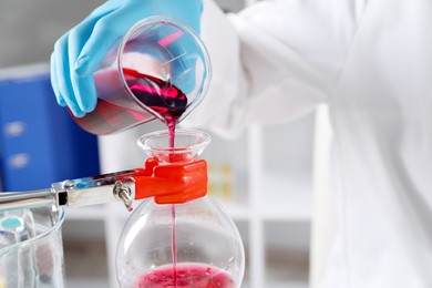 Photo of Scientist pouring sample in glass flask indoors, closeup. Solution chemistry