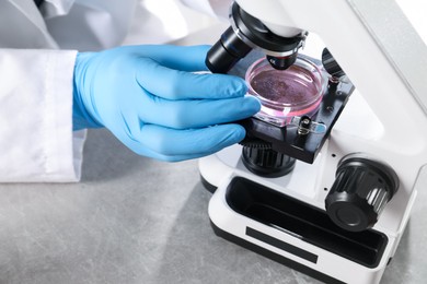 Photo of Scientist examining sample under microscope at grey table in laboratory, closeup. Solution chemistry