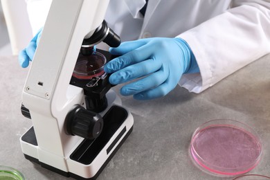 Photo of Scientist examining sample under microscope at grey table in laboratory, closeup. Solution chemistry