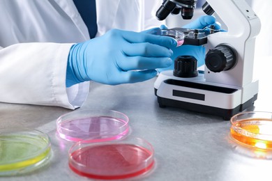 Photo of Scientist examining sample under microscope at grey table in laboratory, closeup. Solution chemistry
