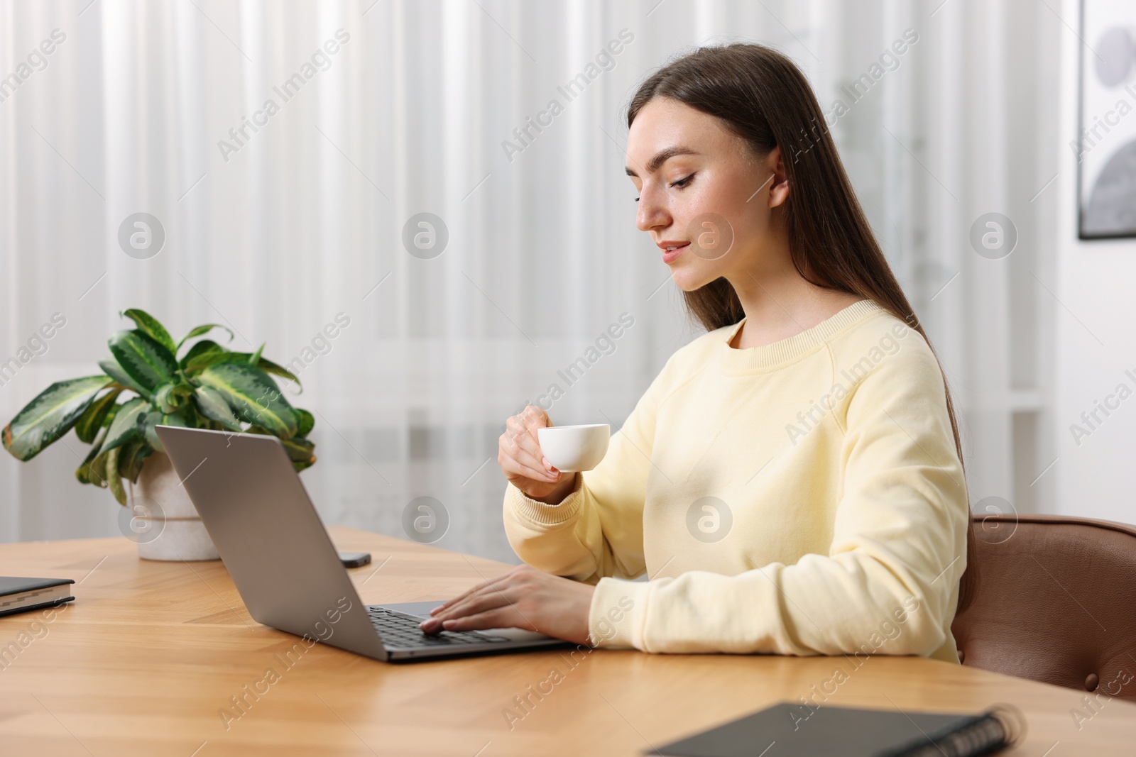 Photo of Copywriter with cup of drink using laptop at wooden table indoors
