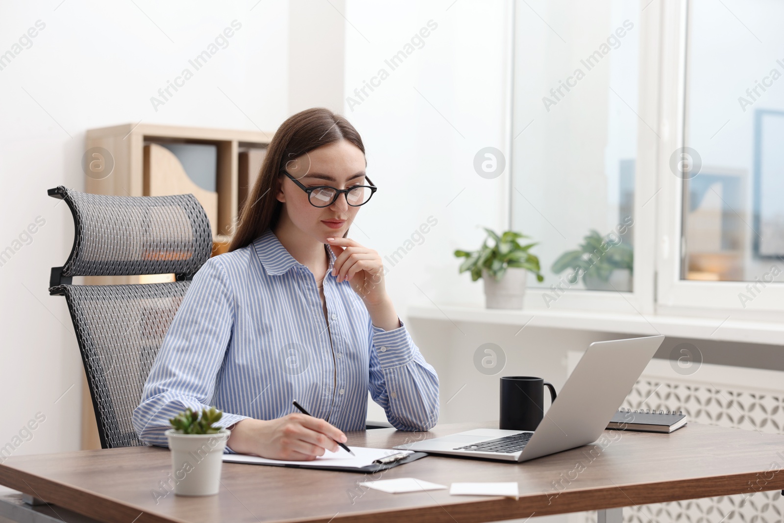 Copywriter using laptop and writing in notebook at wooden table indoors Photo of Copywriter using laptop and writing in notebook at wooden table indoors