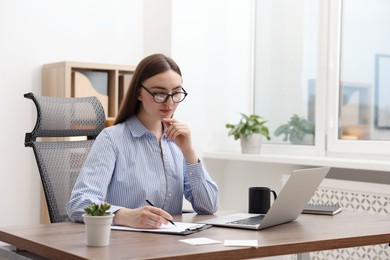 Photo of Copywriter using laptop and writing in notebook at wooden table indoors