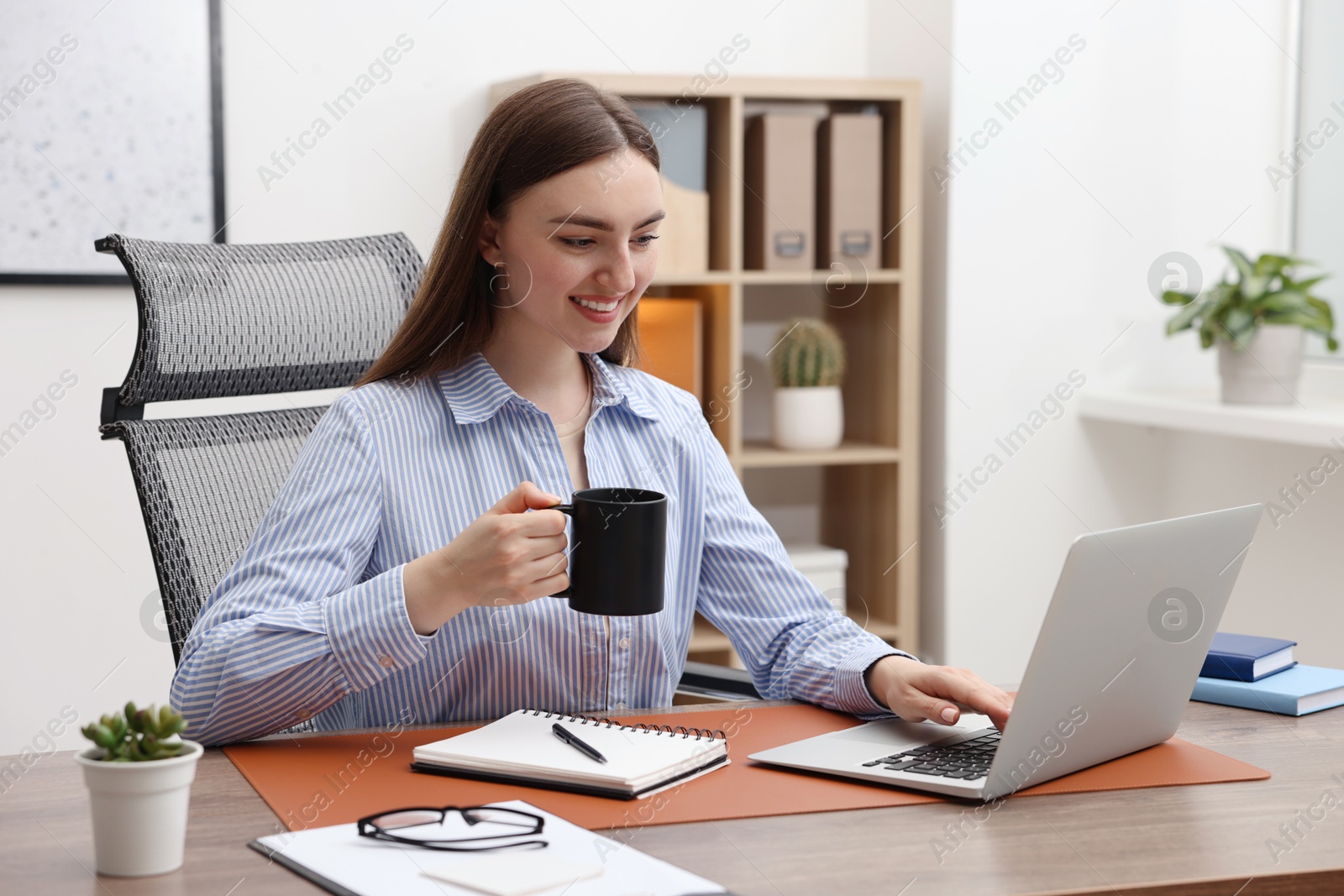 Copywriter with cup of drink using laptop at wooden table indoors Photo of Copywriter with cup of drink using laptop at wooden table indoors