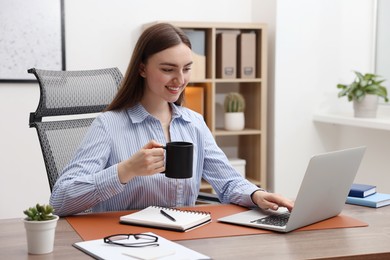Photo of Copywriter with cup of drink using laptop at wooden table indoors