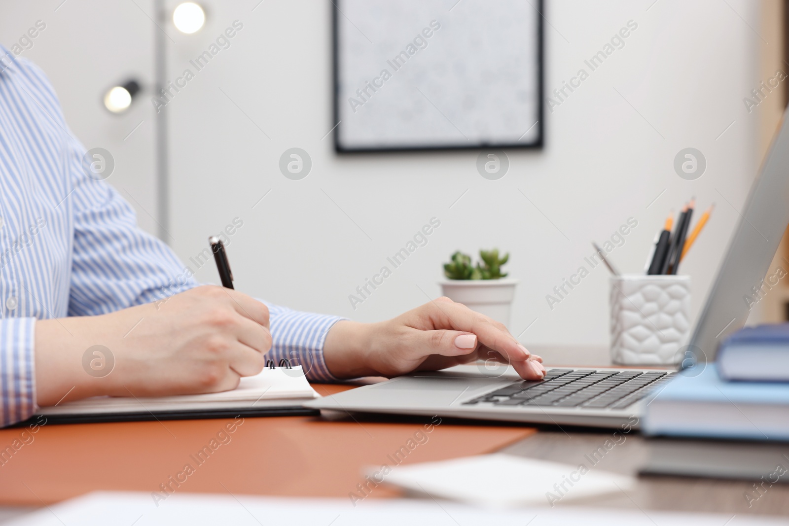 Photo of Copywriter using laptop and writing in notebook at wooden table indoors, closeup