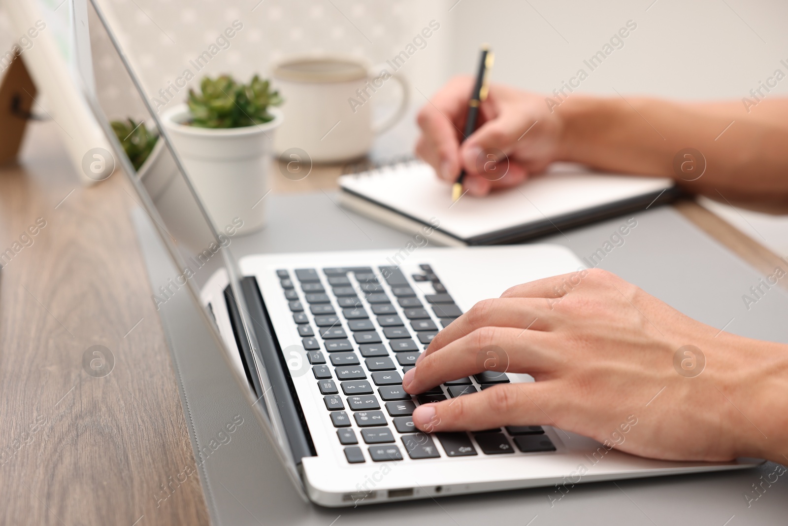 Photo of Copywriter using laptop and writing in notebook at table indoors, closeup