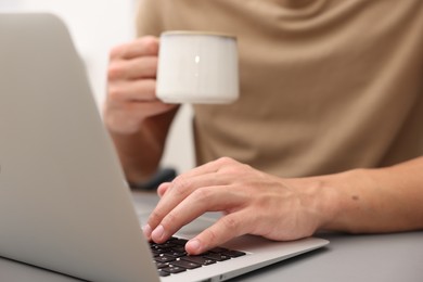 Photo of Copywriter with cup of drink using laptop at wooden table indoors, closeup