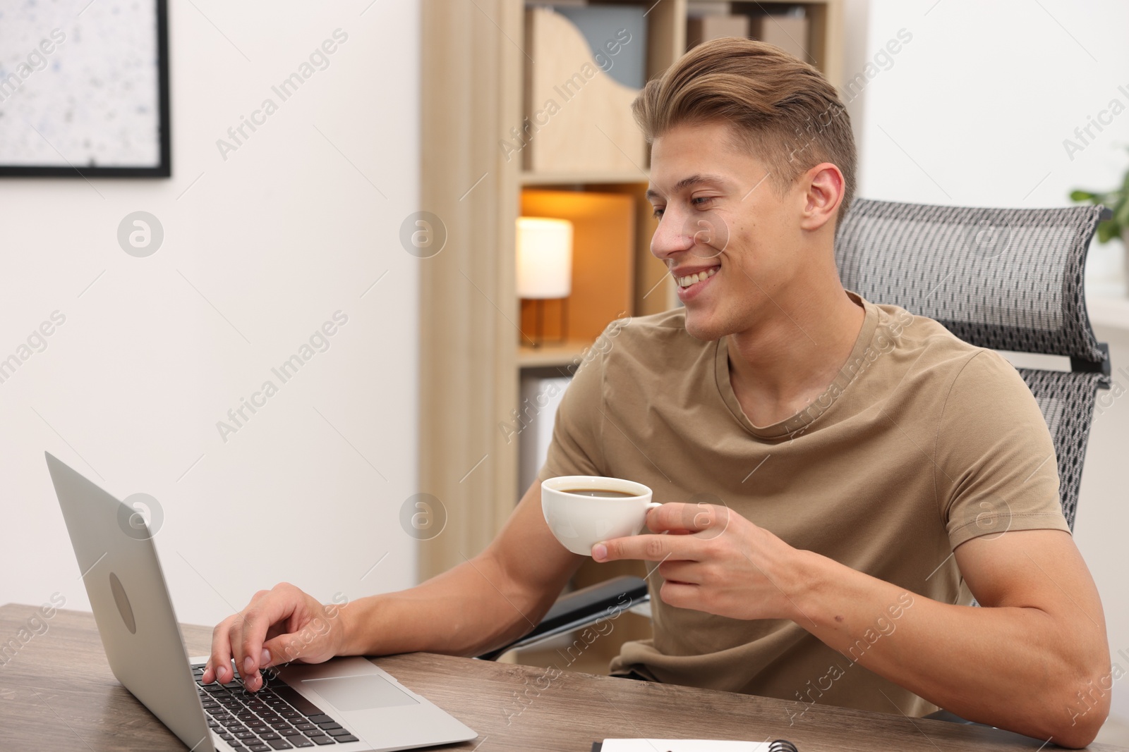 Copywriter with cup of drink using laptop at wooden table indoors Photo of Copywriter with cup of drink using laptop at wooden table indoors