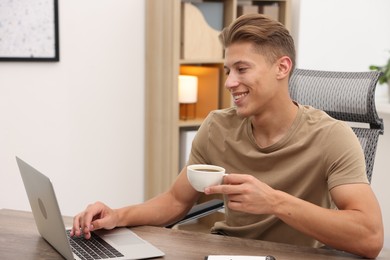 Photo of Copywriter with cup of drink using laptop at wooden table indoors