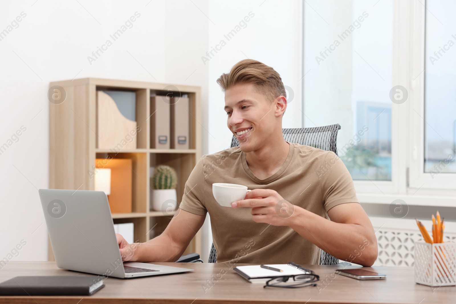 Copywriter with cup of drink using laptop at wooden table indoors Photo of Copywriter with cup of drink using laptop at wooden table indoors