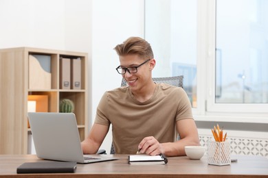 Photo of Copywriter using laptop and writing in notebook at wooden table indoors