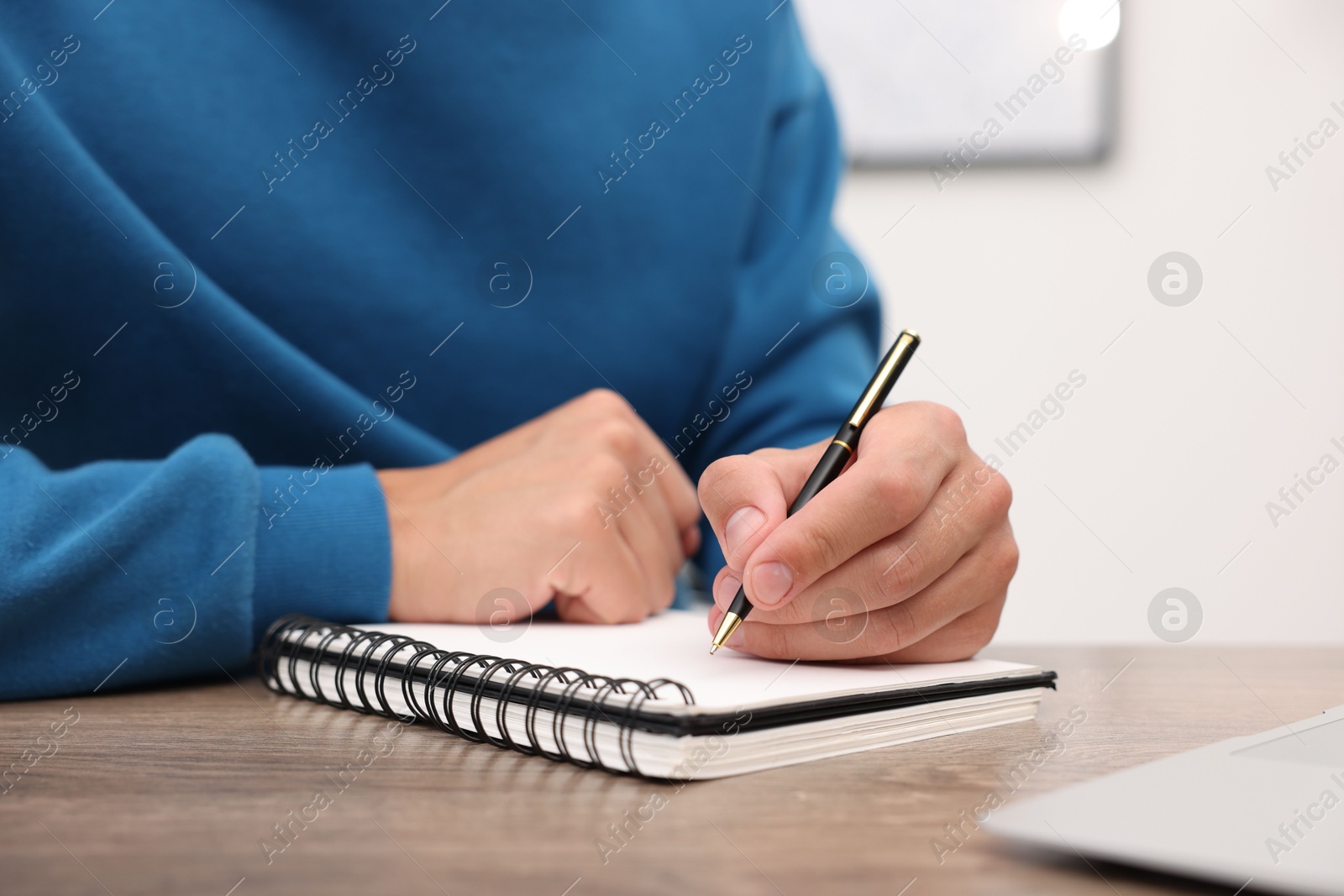 Copywriter with laptop writing in notebook at wooden table indoors, closeup Photo of Copywriter with laptop writing in notebook at wooden table indoors, closeup