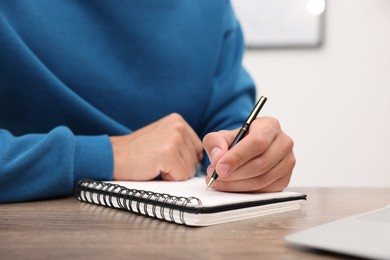 Photo of Copywriter with laptop writing in notebook at wooden table indoors, closeup