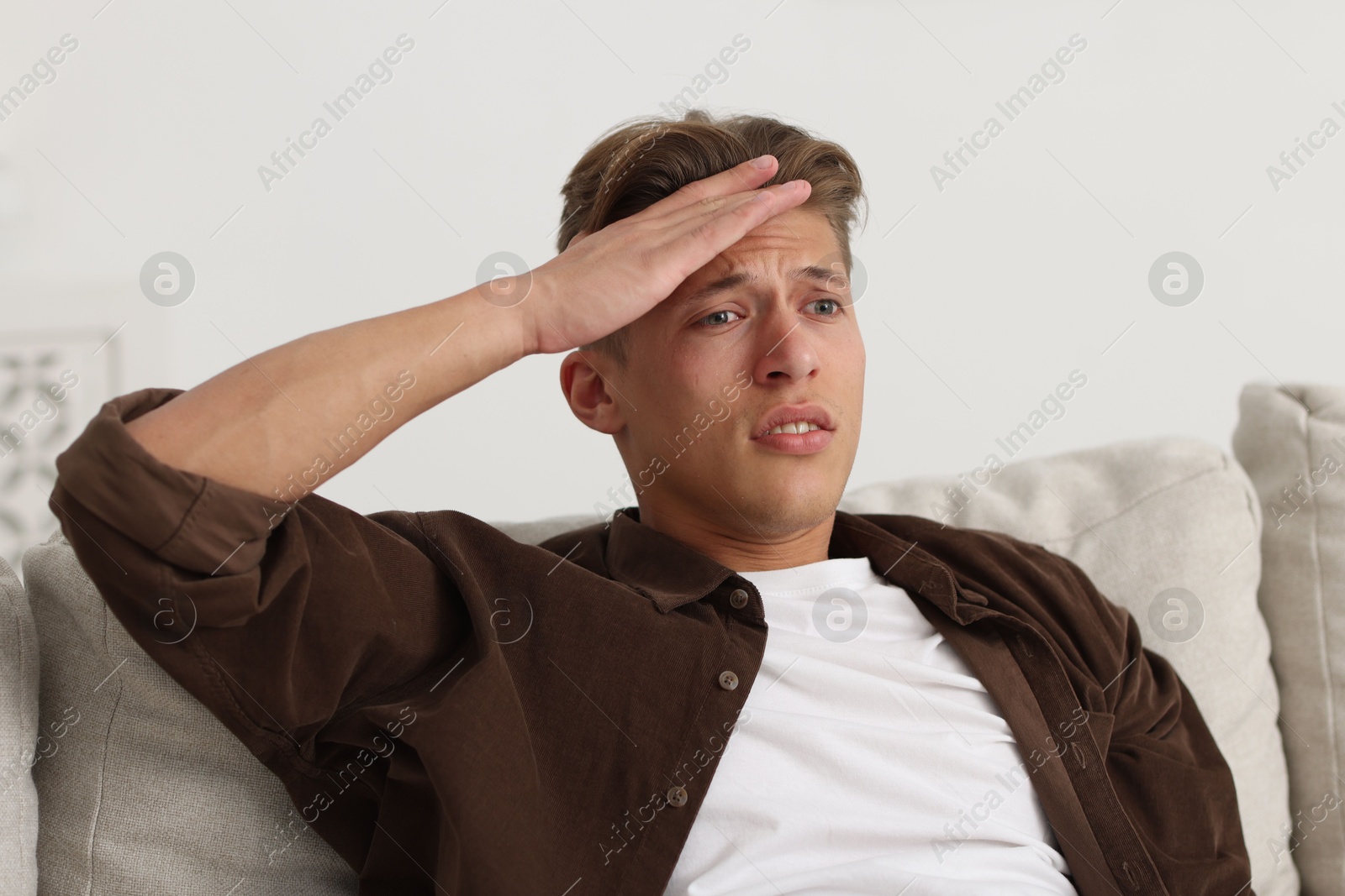 Photo of Young man suffering from headache on sofa at home