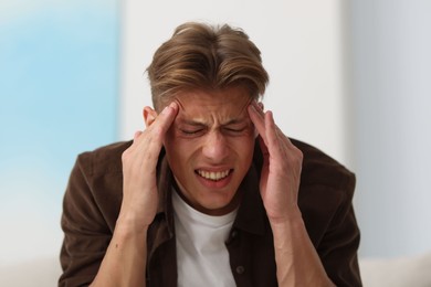 Photo of Young man suffering from headache at home