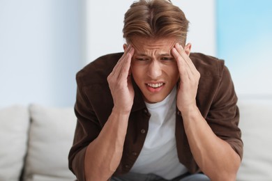 Photo of Young man suffering from headache at home