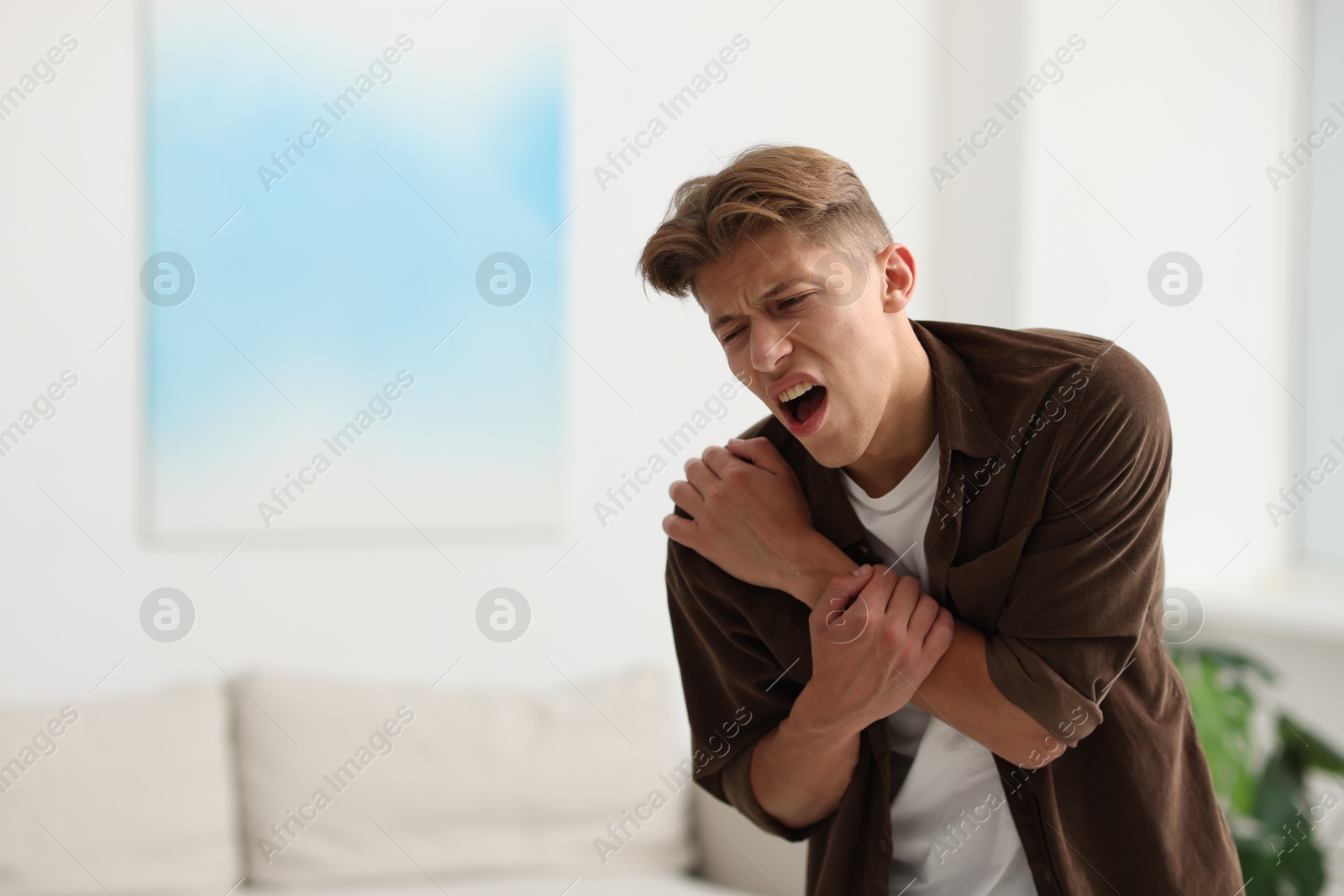 Photo of Young man suffering from shoulder pain at home. Space for text
