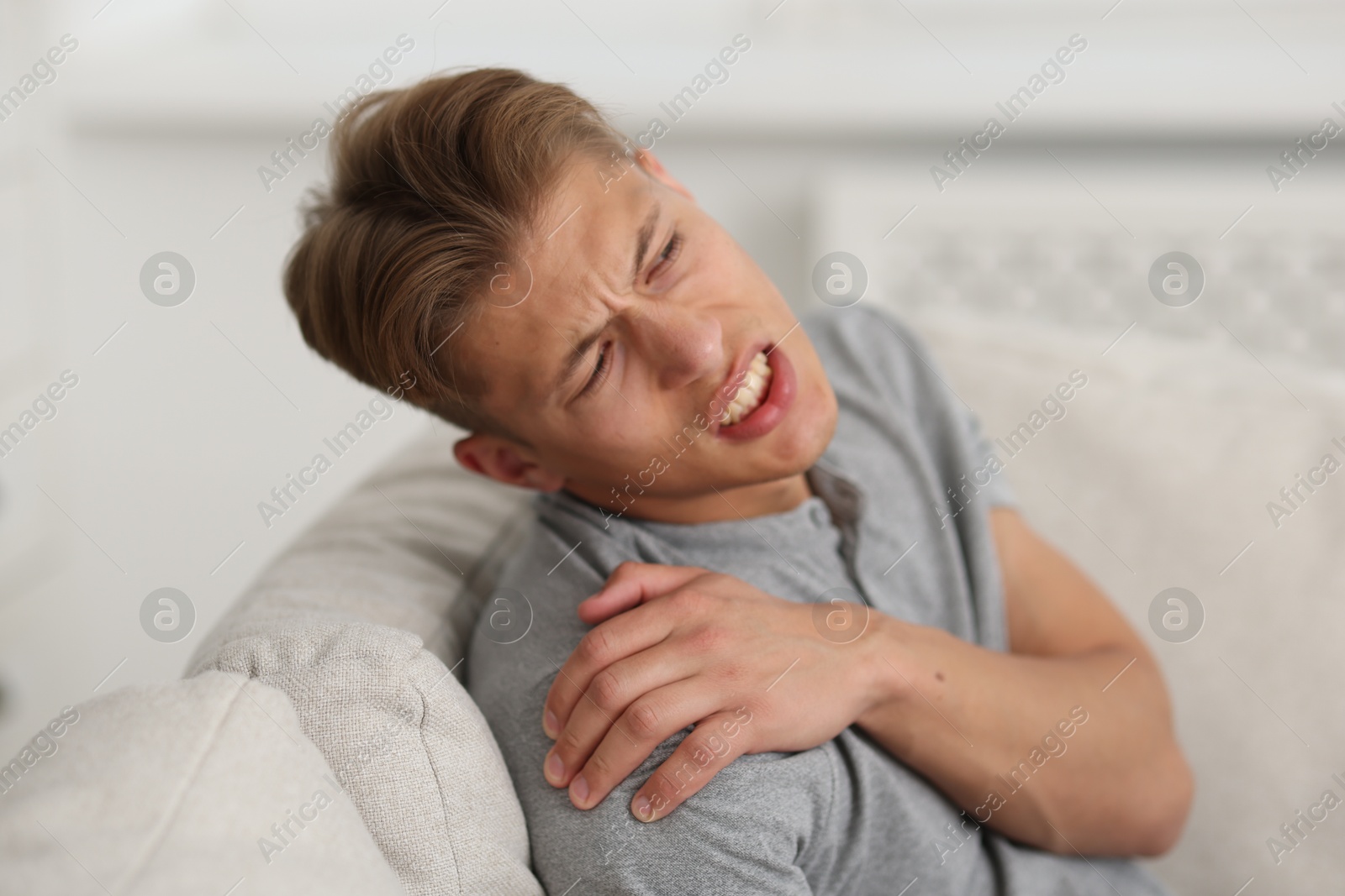 Photo of Young man suffering from shoulder pain on sofa at home