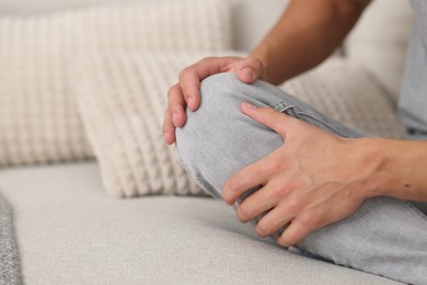 Photo of Man suffering from knee pain on sofa, closeup