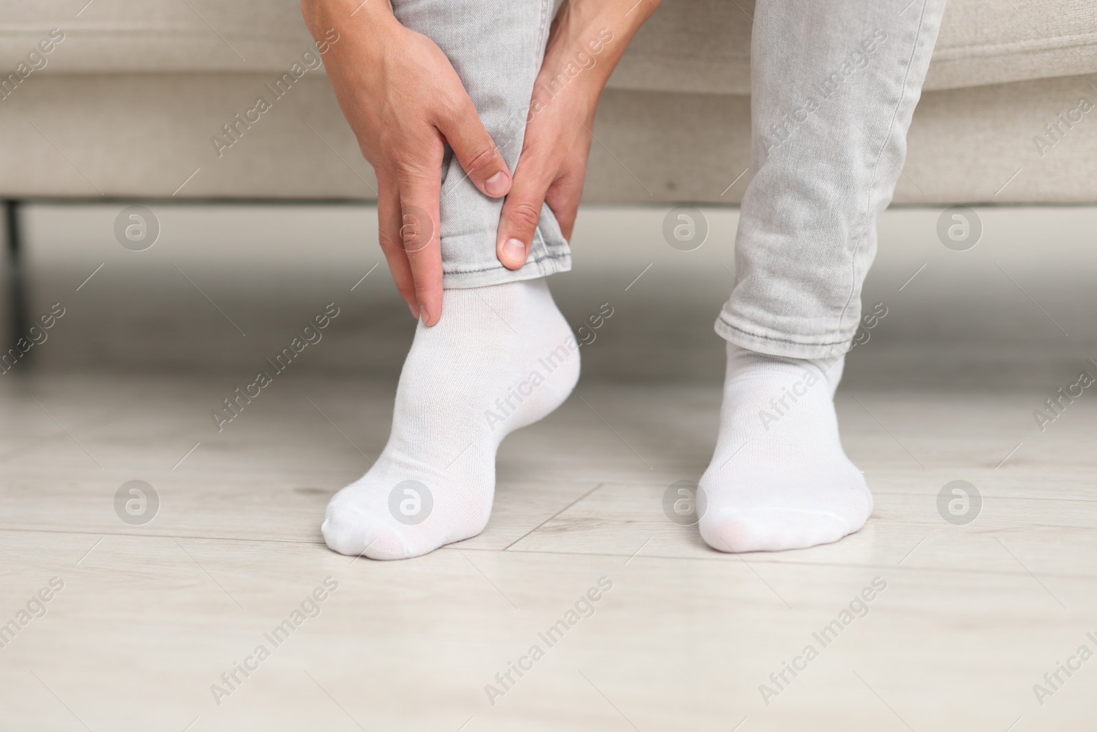 Photo of Man suffering from foot pain on sofa indoors, closeup