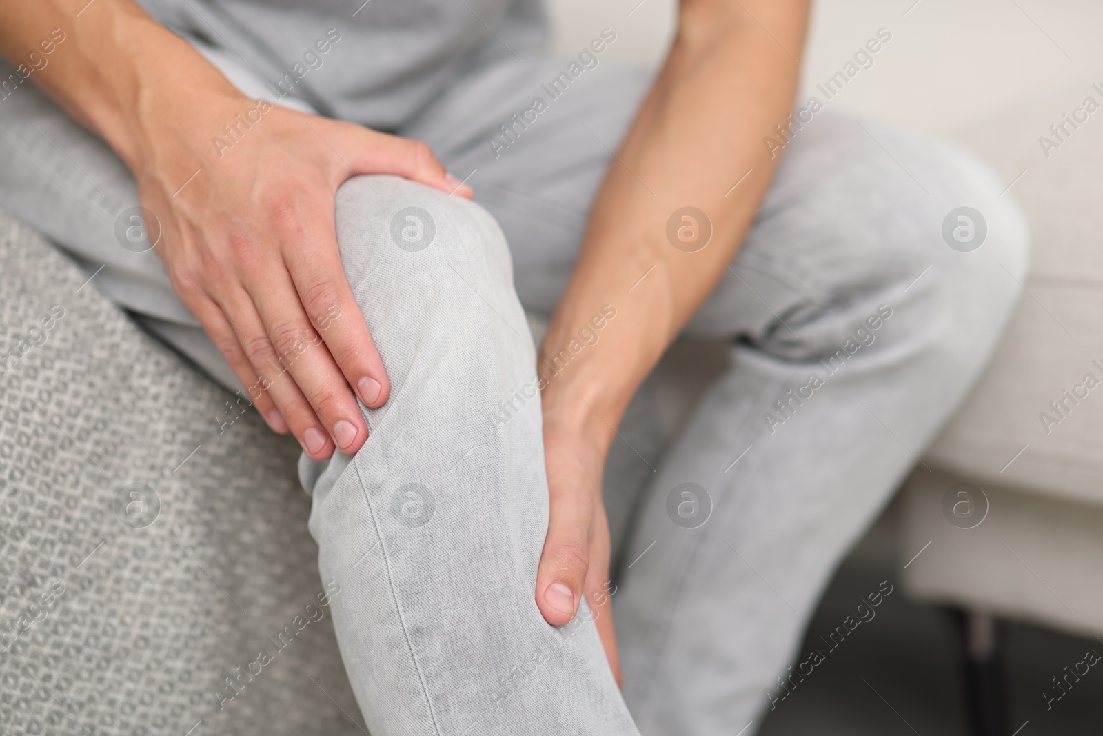 Photo of Man suffering from knee pain on sofa, closeup