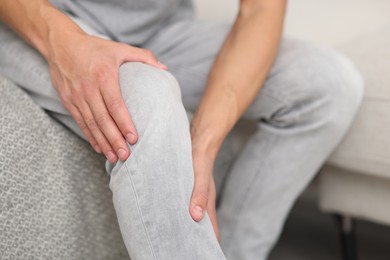 Photo of Man suffering from knee pain on sofa, closeup
