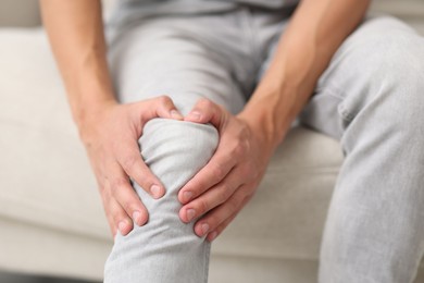 Photo of Man suffering from knee pain on sofa, closeup