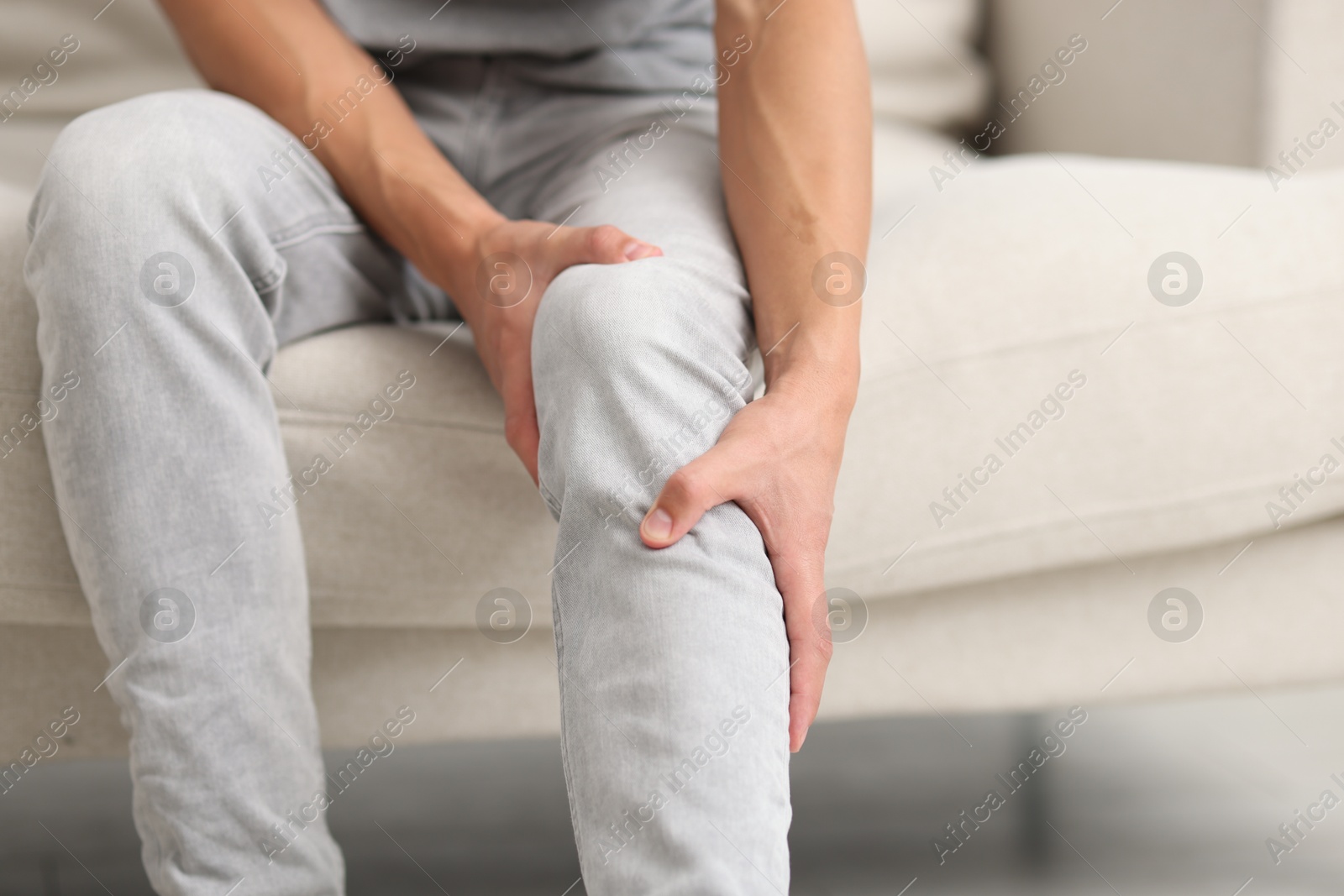 Photo of Man suffering from knee pain on sofa, closeup