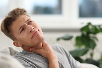 Photo of Young man suffering from sore throat at home. Space for text