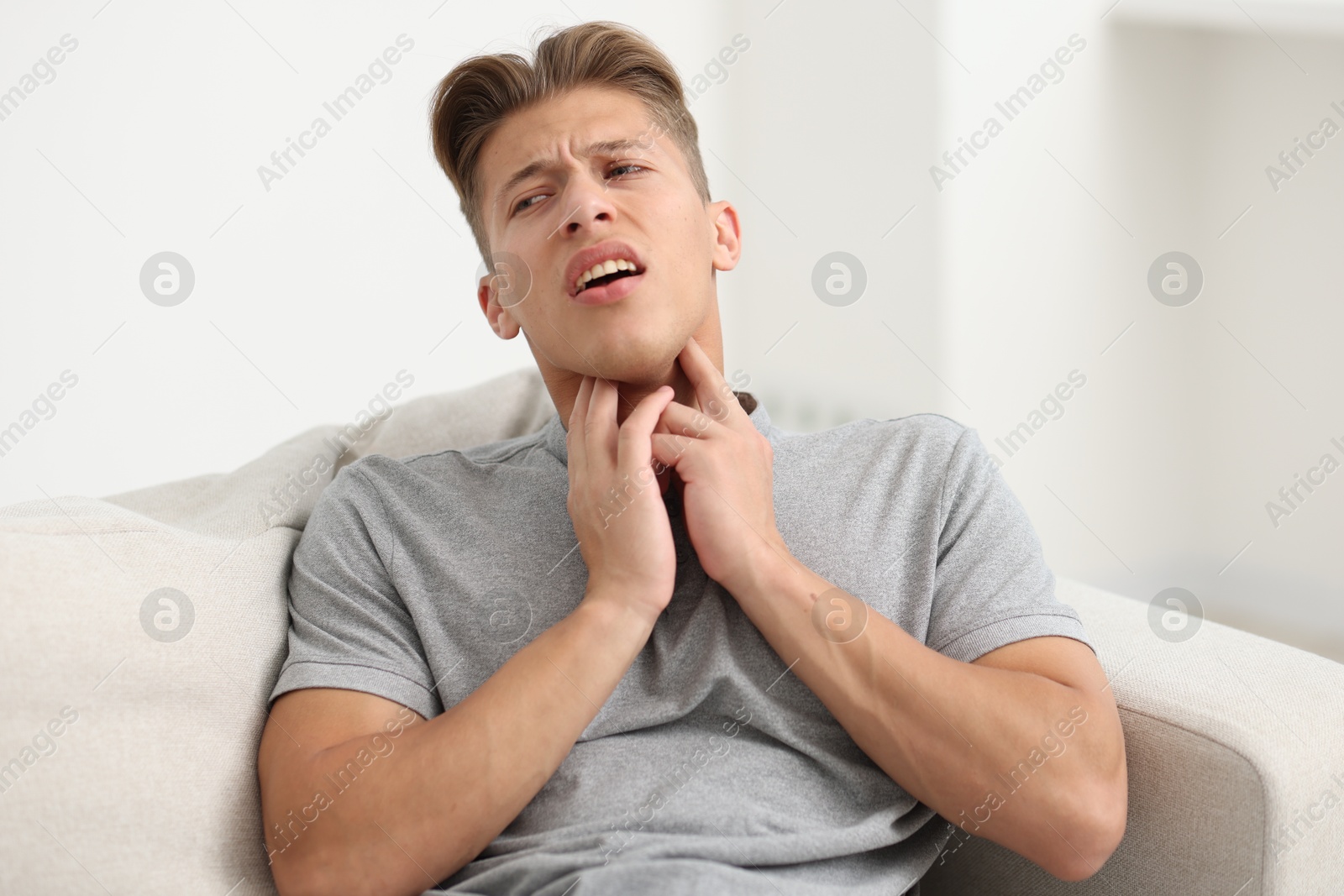 Photo of Young man suffering from sore throat on sofa at home
