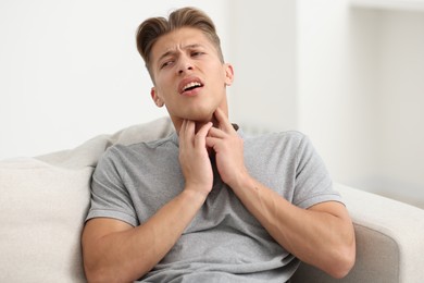 Photo of Young man suffering from sore throat on sofa at home