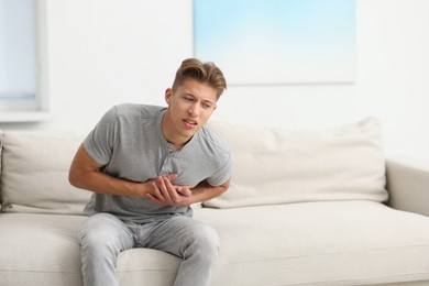 Photo of Young man suffering from chest pain on sofa at home. Space for text