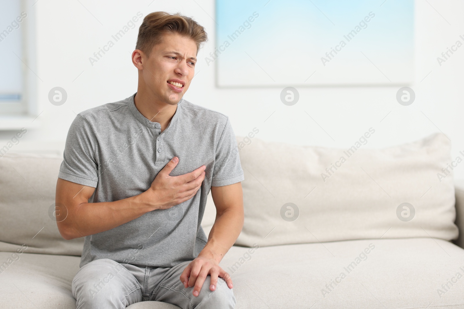 Young man suffering from chest pain on sofa at home. Space for text Photo of Young man suffering from chest pain on sofa at home. Space for text
