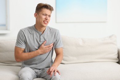 Photo of Young man suffering from chest pain on sofa at home. Space for text