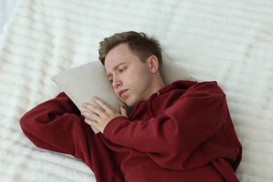 Photo of Sad man with pillow lying on bed, above view. Depression