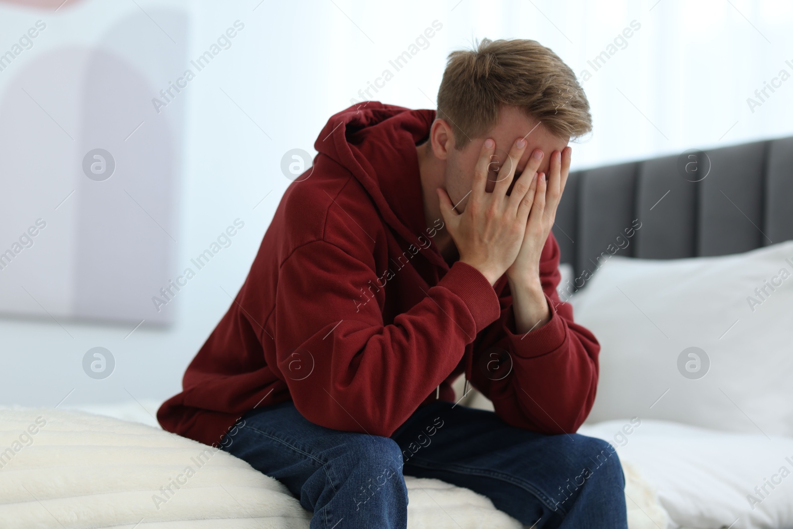 Sad man covering face with hands on bed at home. Depression Photo of Sad man covering face with hands on bed at home. Depression