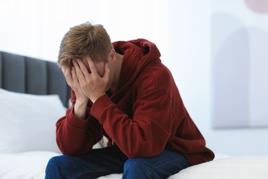 Photo of Sad man covering face with hands on bed at home. Depression